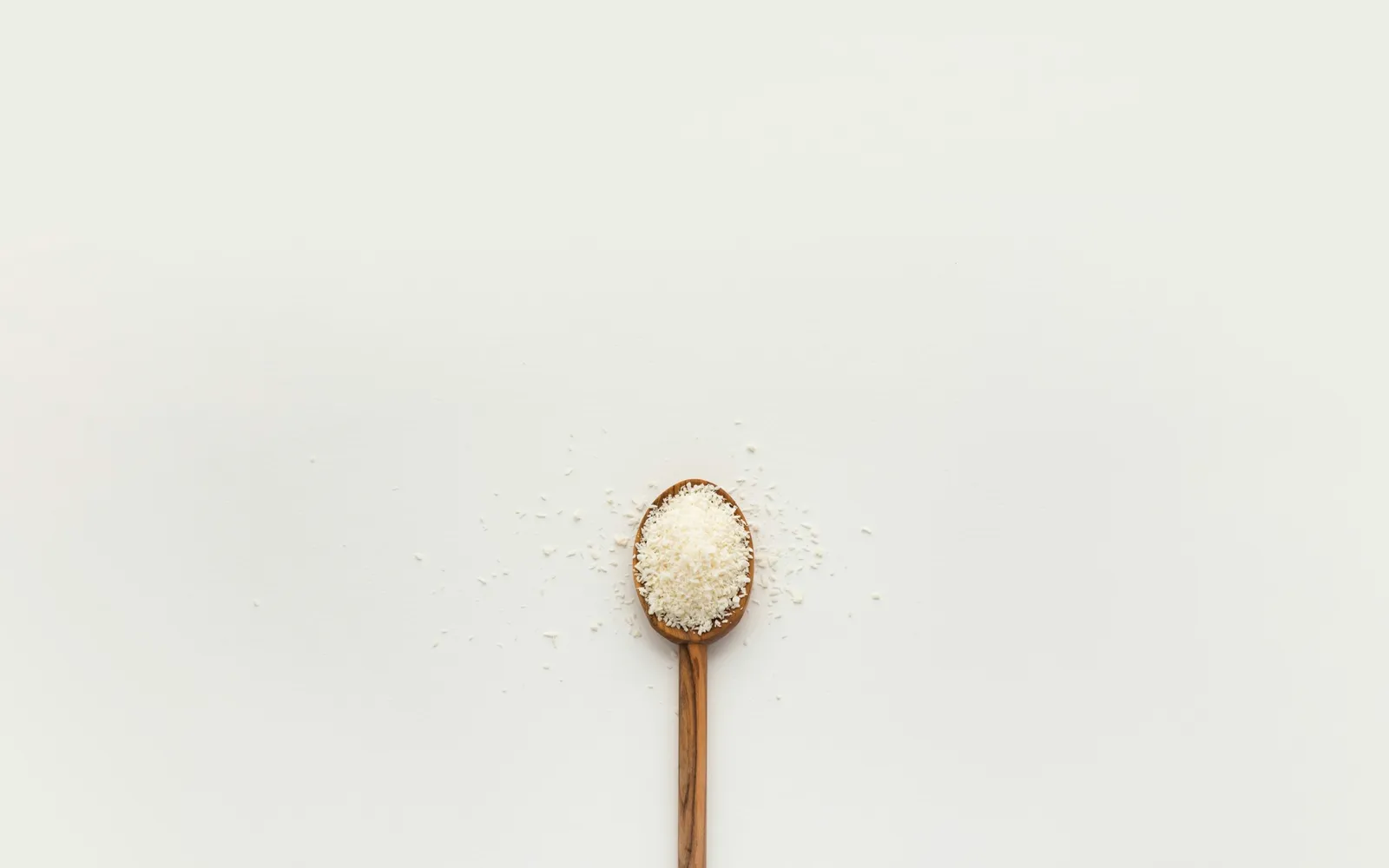 A wooden spoon heaped with white crystals on a plain white surface