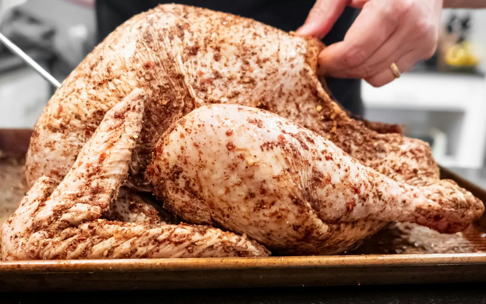 A whole raw turkey rubbed with salt and spices, resting on a sheet pan